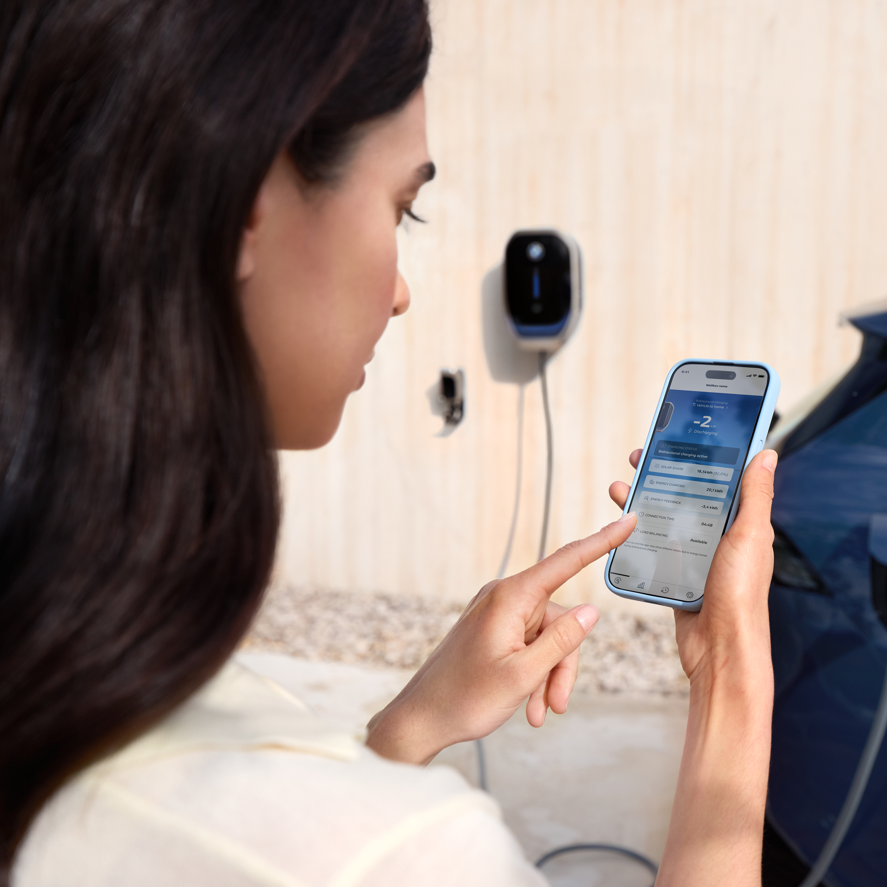 Жена гледа в смартфона си, на заден план е BMW Wallbox