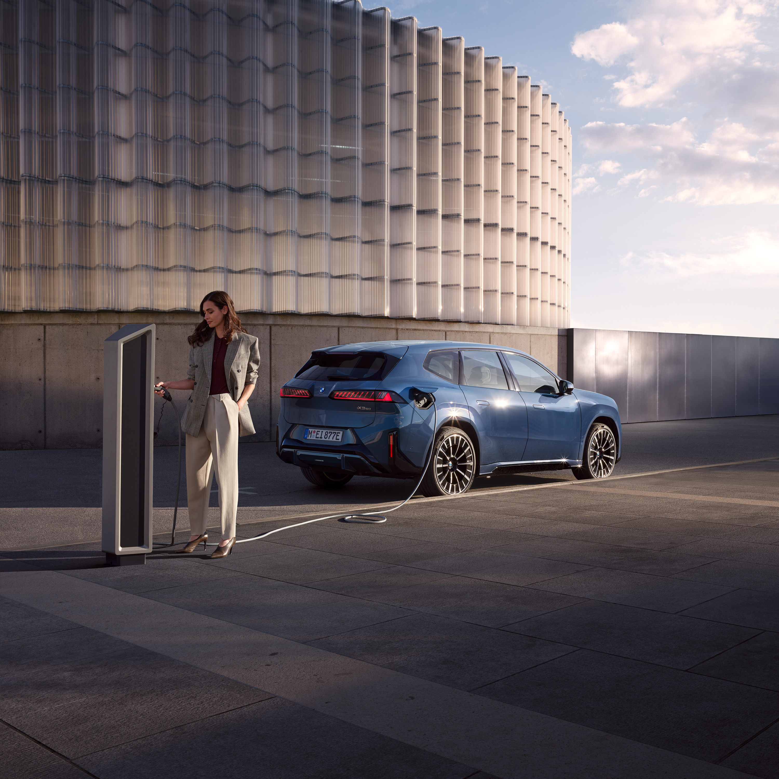 Мъж стои до BMW iX 3, което е свързано към обществена зарядна колонка
