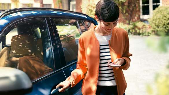 Жена гледа смартфона си и отваря вратата на своето BMW BMW Телеуслуги жена гледа смартфона си и отваря вратата на своето BMW