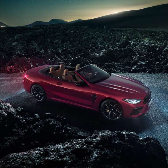 BMW M8 Competition Кабриолет в цвят Motegi Red metallic, три четвърти изглед отстрани. BMW M8 Competition Кабриолет в цвят Motegi Red metallic с отворен мек покрив, три четвърти изглед отстрани, в покой през нощта на асфалтов път.