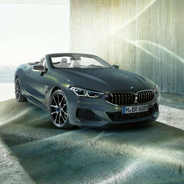 BMW M850i xDrive Кабриолет, три четвърти изглед отпред. BMW M850i xDrive Кабриолет в цвят Dravit Grey metallic с отворен мек покрив, три четвърти изглед отпред, в покой на брега.
