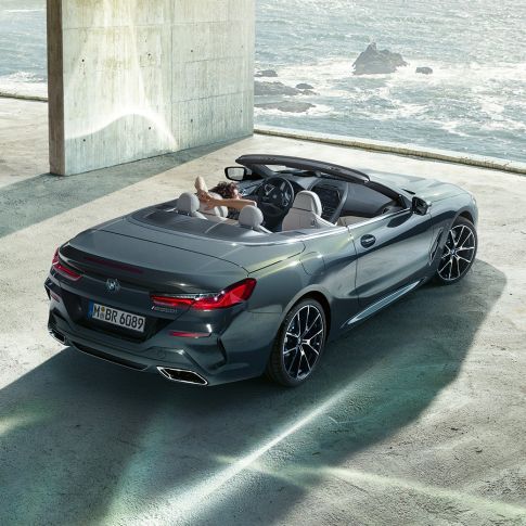 BMW M850i xDrive Кабриолет, от перспектива „птичи поглед“. BMW M850i xDrive Кабриолет в цвят Dravit Grey metallic с отворен мек покрив, от перспектива „птичи поглед“, паркирано в бетонна сграда на фона на океана.