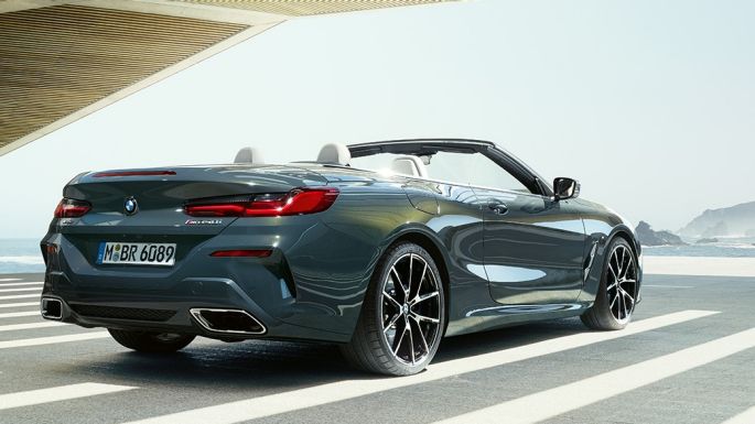 BMW M850i xDrive Кабриолет, три четвърти изглед отзад. BMW M850i xDrive Кабриолет в цвят Dravit Grey metallic с отворен мек покрив, три четвърти изглед отзад, паркирано с изглед към океана.
