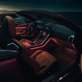 BMW M8 Competition Кабриолет, интериор. BMW M8 Competition Кабриолет с отворен мек покрив, интериор с червено вътрешно осветление през нощта.