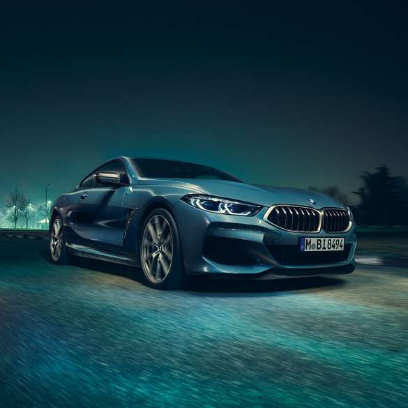 BMW M850i xDrive Купе, три четвърти изглед отпред вляво. BMW M850i xDrive Купе в Barcelona Blue metallic, три четвърти изглед отпред вляво в движение през нощта.