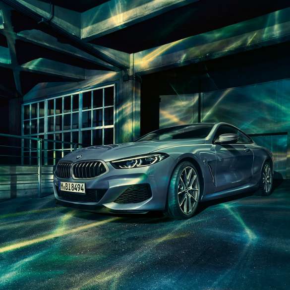 BMW M850i xDrive Купе, три четвърти изглед отпред. BMW M850i xDrive Купе в Barcelona Blue metallic, три четвърти изглед отпред в покой пред сграда.