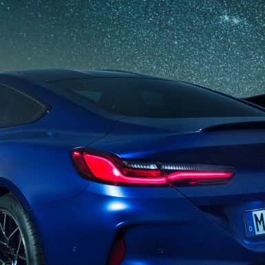 М Заден спойлер BMW M8 Competition Купе в Marina Bay Blue metallic, снимка отблизо на областта на раменете през нощта с М заден спойлер от карбон.