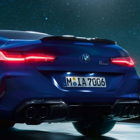 Черен карбонов М дифузор. BMW M8 Competition Купе в Marina Bay Blue metallic, снимка отблизо на задната част през нощта с черен карбонов М дифузор.