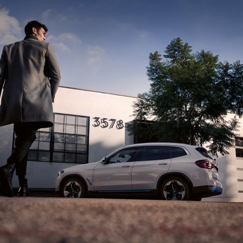 BMW iX3 G08 изглед отстрани пред сграда с мъж BMW iX3 G08 2020 Mineral White metallic изглед отстрани пред сграда с мъж