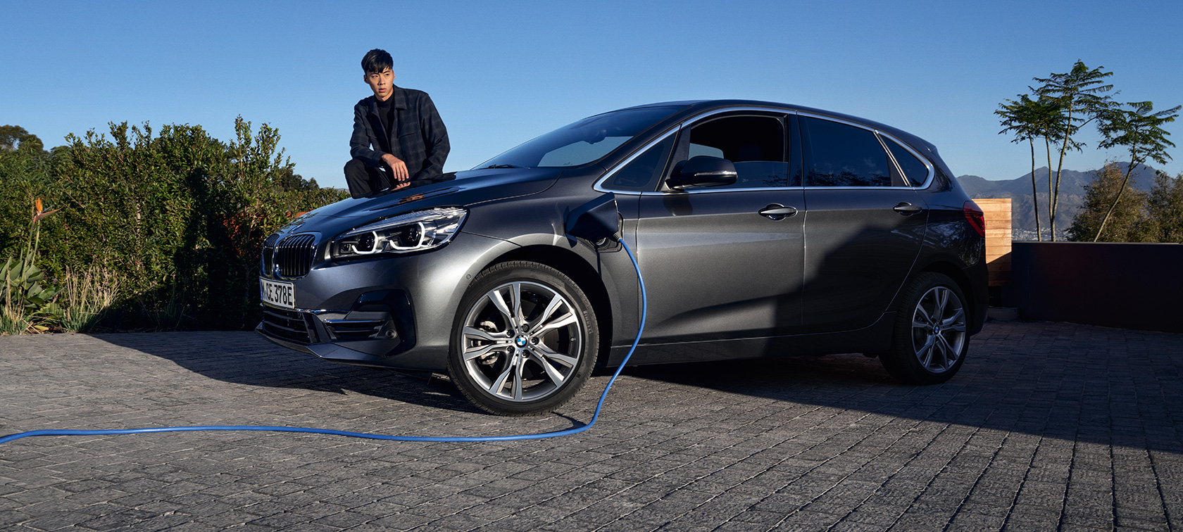 Plug-in хибрид BMW 225xe Актив Турър F45 три четвърти изглед отстрани при зареждане Plug-in хибрид BMW 225xe Актив Турър F45 три четвърти изглед отстрани при зареждане с модел