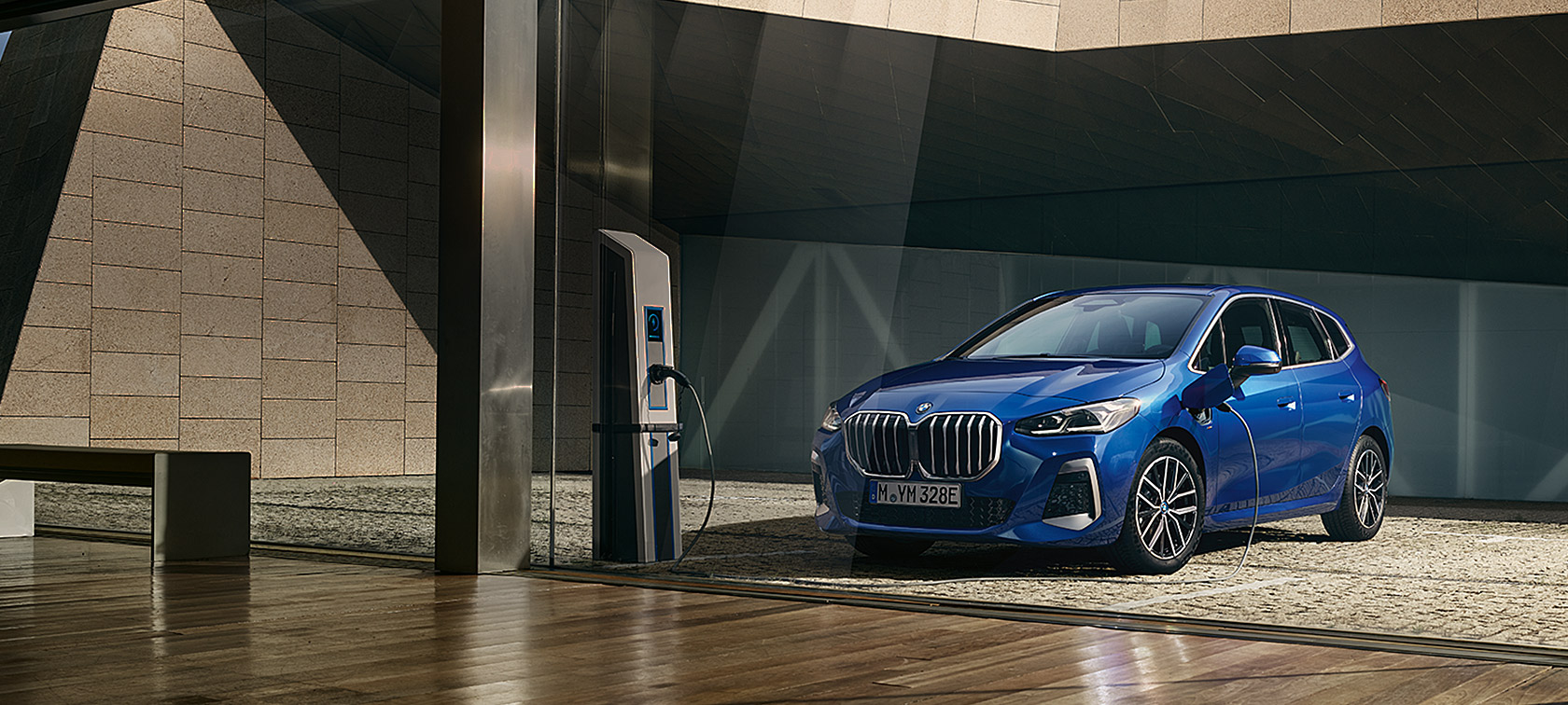 BMW Серия 2 Актив Турър 230e Plug-in хибрид U06 2021 M Portimao Blue metallic три четвърти изглед отпред на зарядна станция