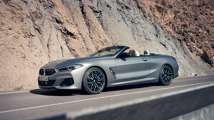 Новото BMW Серия 8 Кабриолет G14 LCI фейслифт 2022 с отворен покрив в движение на фона на планини Новото BMW Серия 8 Кабриолет G14 LCI фейслифт 2022 BMW Individual Frozen Pure Grey metallic изглед отстрани с отворен покрив в движение на фона на планини