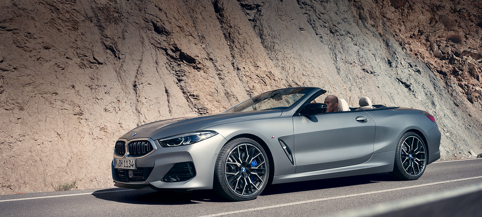 Новото BMW Серия 8 Кабриолет G14 LCI фейслифт 2022 изглед отстрани с отворен покрив в движение на фона на планини Новото BMW Серия 8 Кабриолет G14 LCI фейслифт 2022 BMW Individual Frozen Pure Grey metallic изглед отстрани с отворен покрив в движение на фона на планини