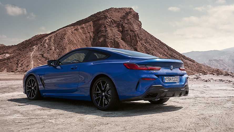 Три четвърти изглед отстрани BMW Серия 8 Купе М Спортен пакет G15 LCI Facelift 2022 BMW Серия 8 Купе М Спортен пакет G15 LCI Facelift 2022 М Portimao Blue metallic три четвърти изглед отзад в покой през скали