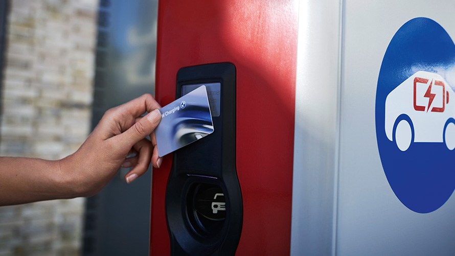 Човек държи BMW Charging Card до обществена зарядна станция Човек държи BMW Charging Card до обществена зарядна станция