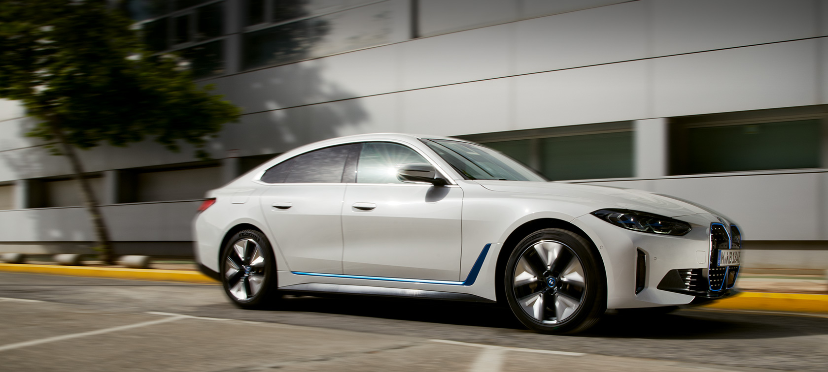 BMW i4 eDrive40 G26 2021 Mineral White три четвърти изглед отстрани в движение пред сграда BMW i4 eDrive40 G26 2021 Mineral White три четвърти изглед отпред в движение пред сграда