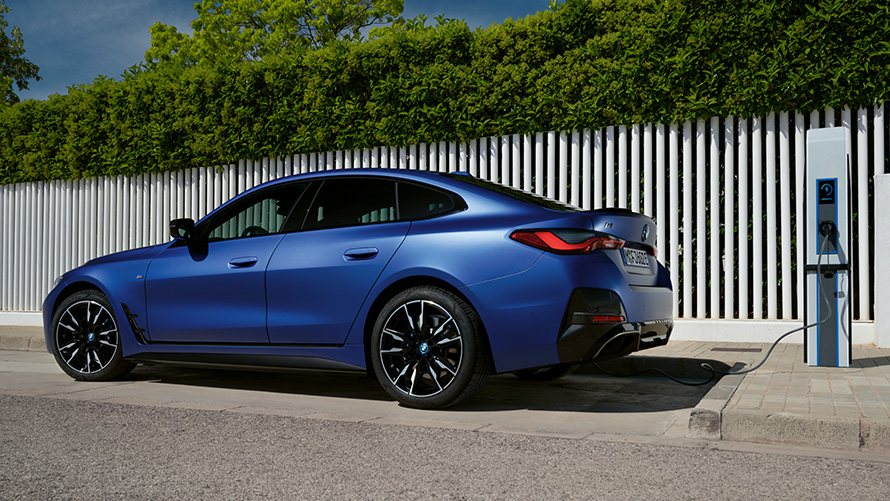 Изглед отстрани BMW i4 M50 G26 2021 на обществена бърза зарядна станция BMW i4 M50 G26 2021 BMW Individual Frozen Portimao Blue metallic изглед отстрани на обществена бърза зарядна станция