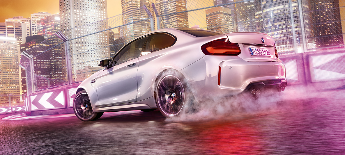 BMW M2 Competition ускорява. Бяло BMW M2 Compeititon дрифтира на състезателна писта.