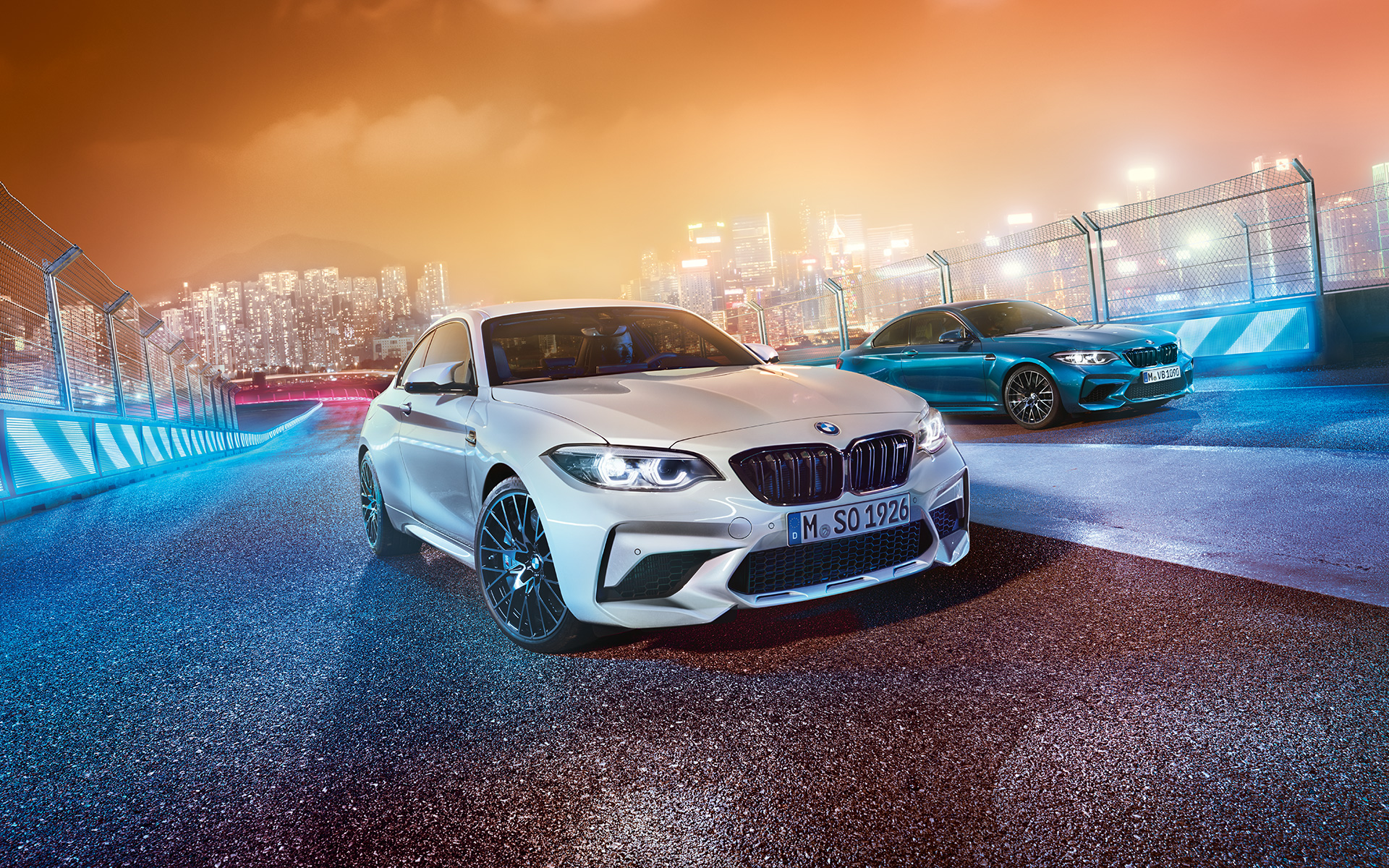 Два автомобила BMW M2 Competition на състезателна писта Бяло и синьо BMW M2 Compeititon в покой на състезателна писта.