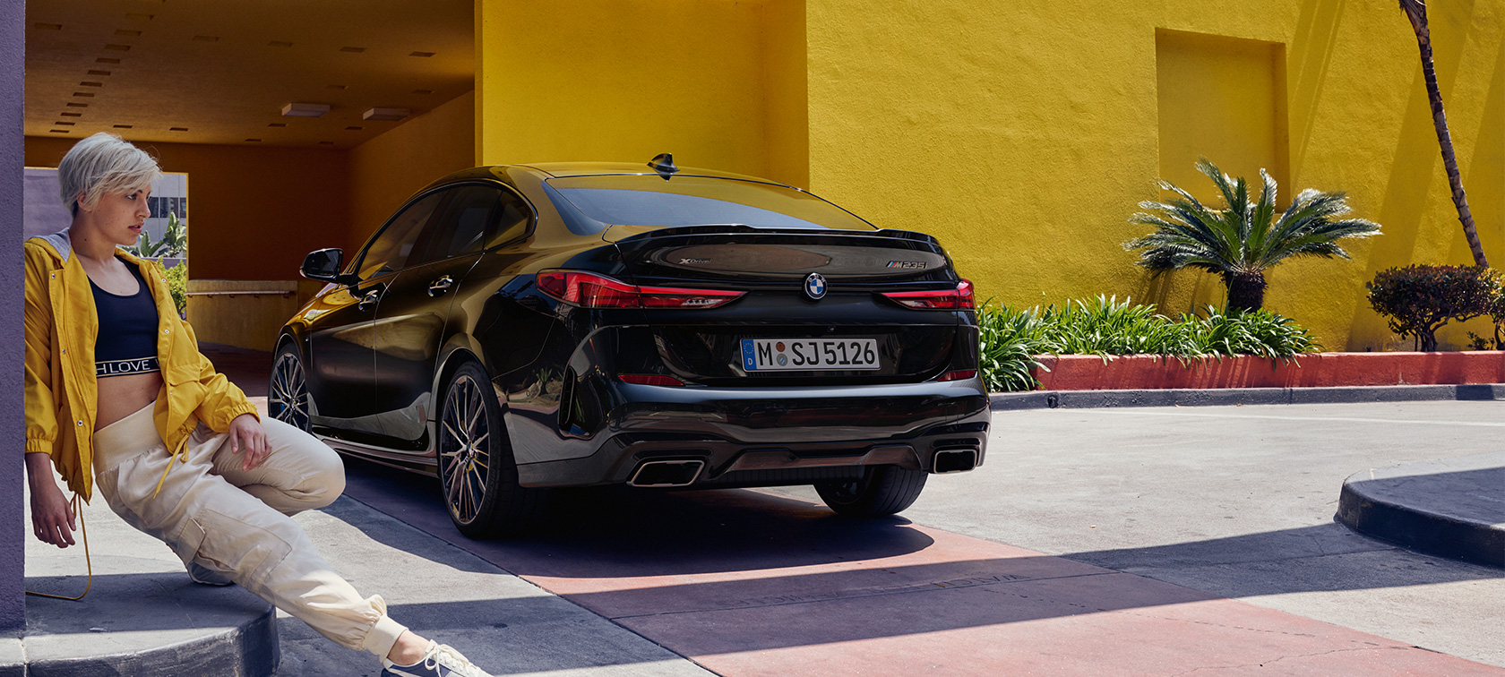 BMW M235i xDrive Гран Купе три четвърти отзад BMW M235i xDrive Гран Купе Black Sapphire metallic F44 три четвърти отзад с жена на преден план