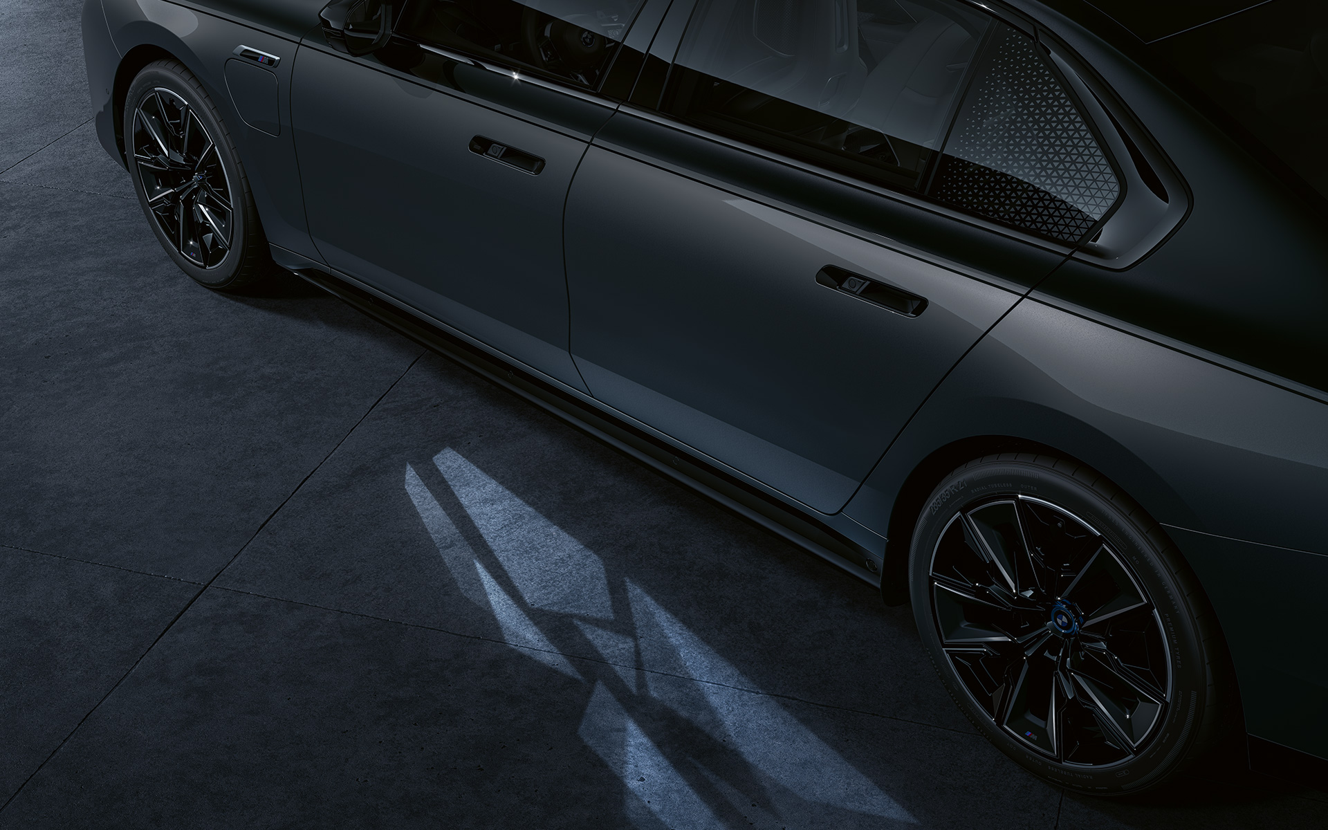 Светлинна концепция BMW M760e xDrive G70 Two-Tone лаково покритие Saphire Black metallic BMW Individual Dravite Grey metallic изглед отблизо отстрани с включен Welcome Light Carpet