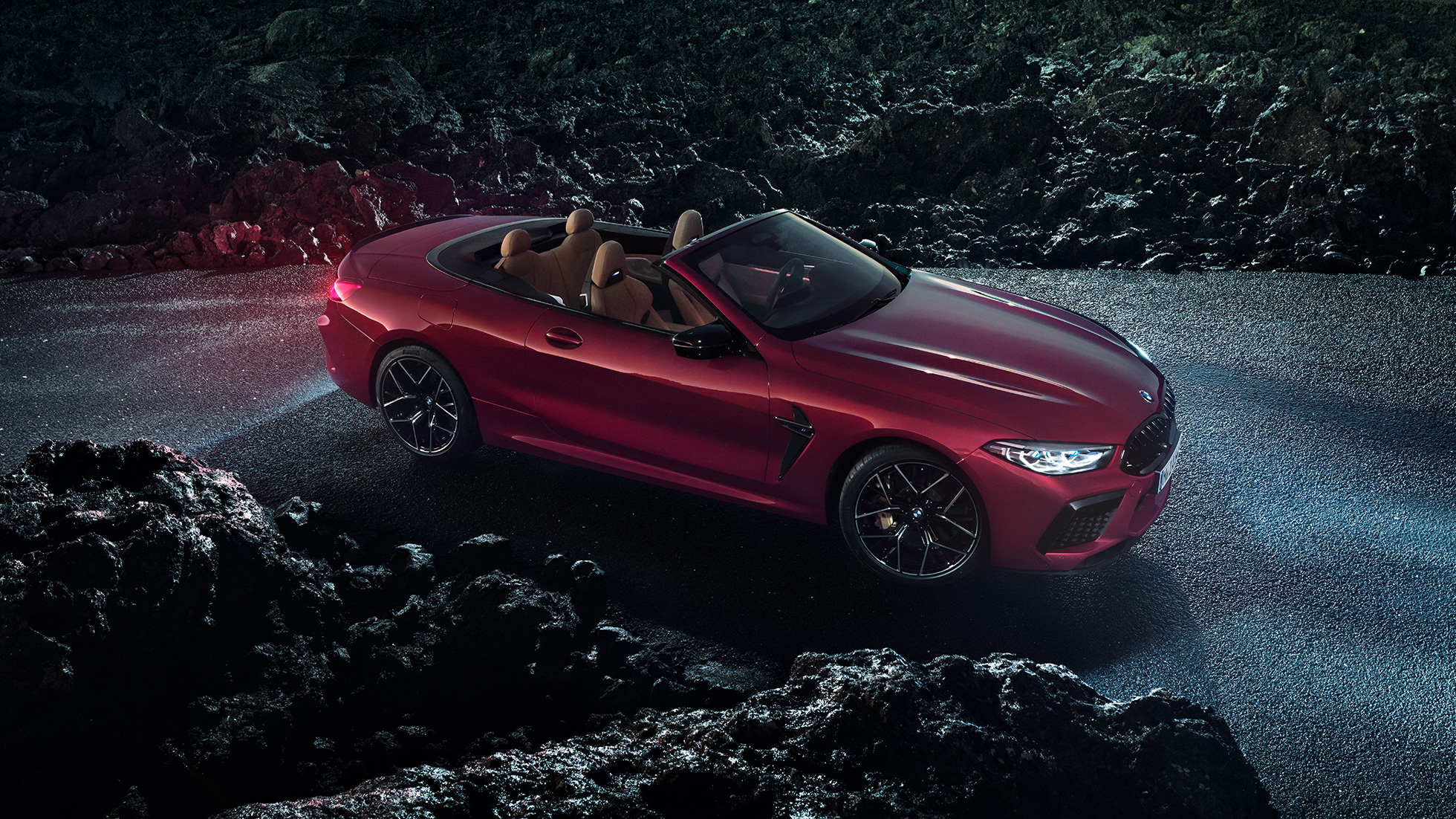BMW M8 Competition Кабриолет в цвят Motegi Red metallic, три четвърти изглед отстрани. BMW M8 Competition Кабриолет в цвят Motegi Red metallic с отворен мек покрив, три четвърти изглед отстрани, в покой през нощта на асфалтов път.