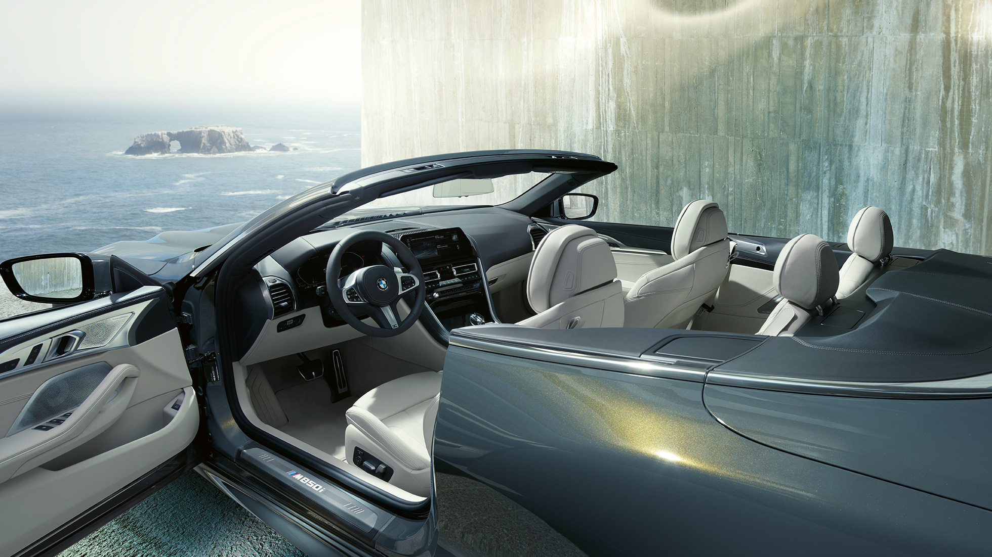 BMW M850i xDrive Кабриолет, интериор. BMW M850i xDrive Кабриолет в цвят Dravit Grey metallic с отворен мек покрив, интериор с М кожен волан и кожена тапицерия BMW Individual 'Merino' Ivory White.