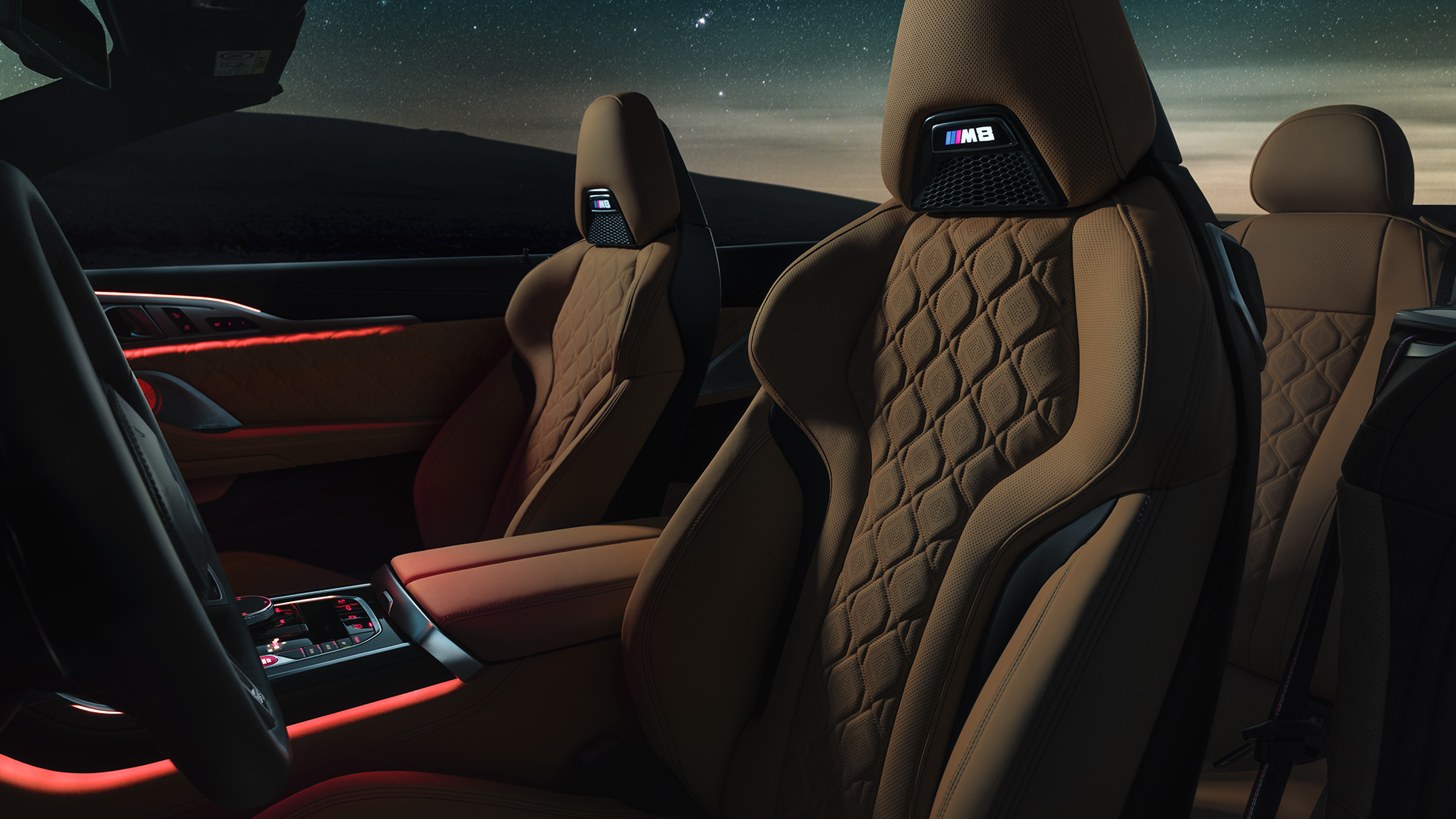 М Спортни седалки с кожена тапицерия 'Merino'. BMW M8 Competition Кабриолет с отворен мек покрив под звездно небе, интериор с М Спортни седалки с кожена тапицерия 'Merino' и червено вътрешно осветление.