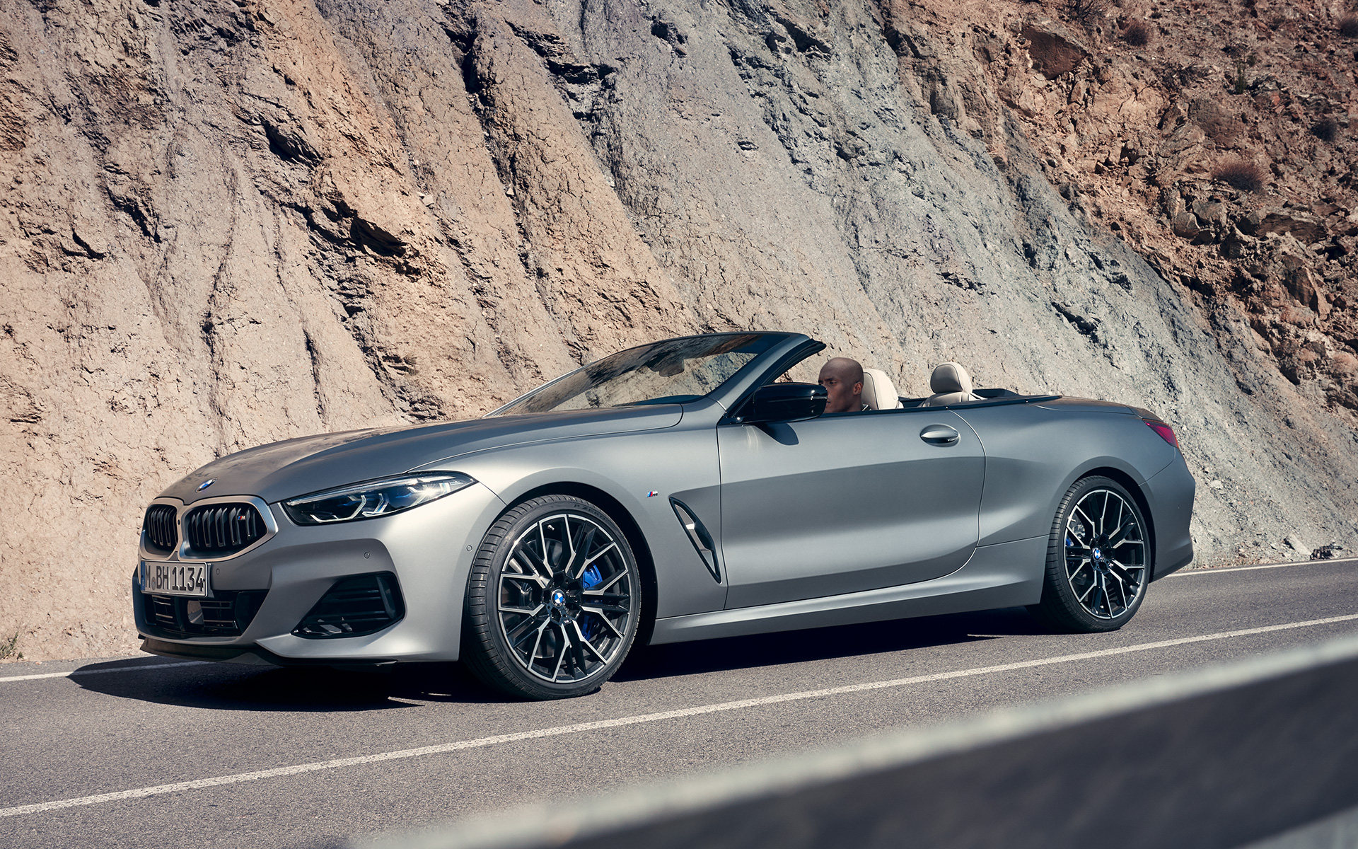 Три-четвърти изглед отпред BMW M850i xDrive Кабриолет G14 LCI Facelift 2022 BMW M850i xDrive Кабриолет G14 LCI Facelift 2022 BMW Individual Frozen Pure Grey metallic три-четвърти изглед отпред в движение пред скала