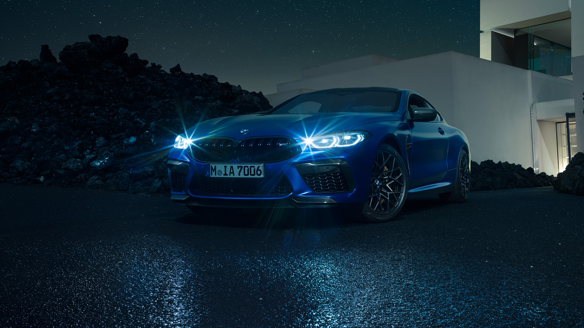 BMW M8 Competition Купе, три четвърти изглед отпред. BMW M8 Competition Купе в Marina Bay Blau metallic ярки LED фарове, три четвърти изглед отпред в покой пред вила през нощта.
