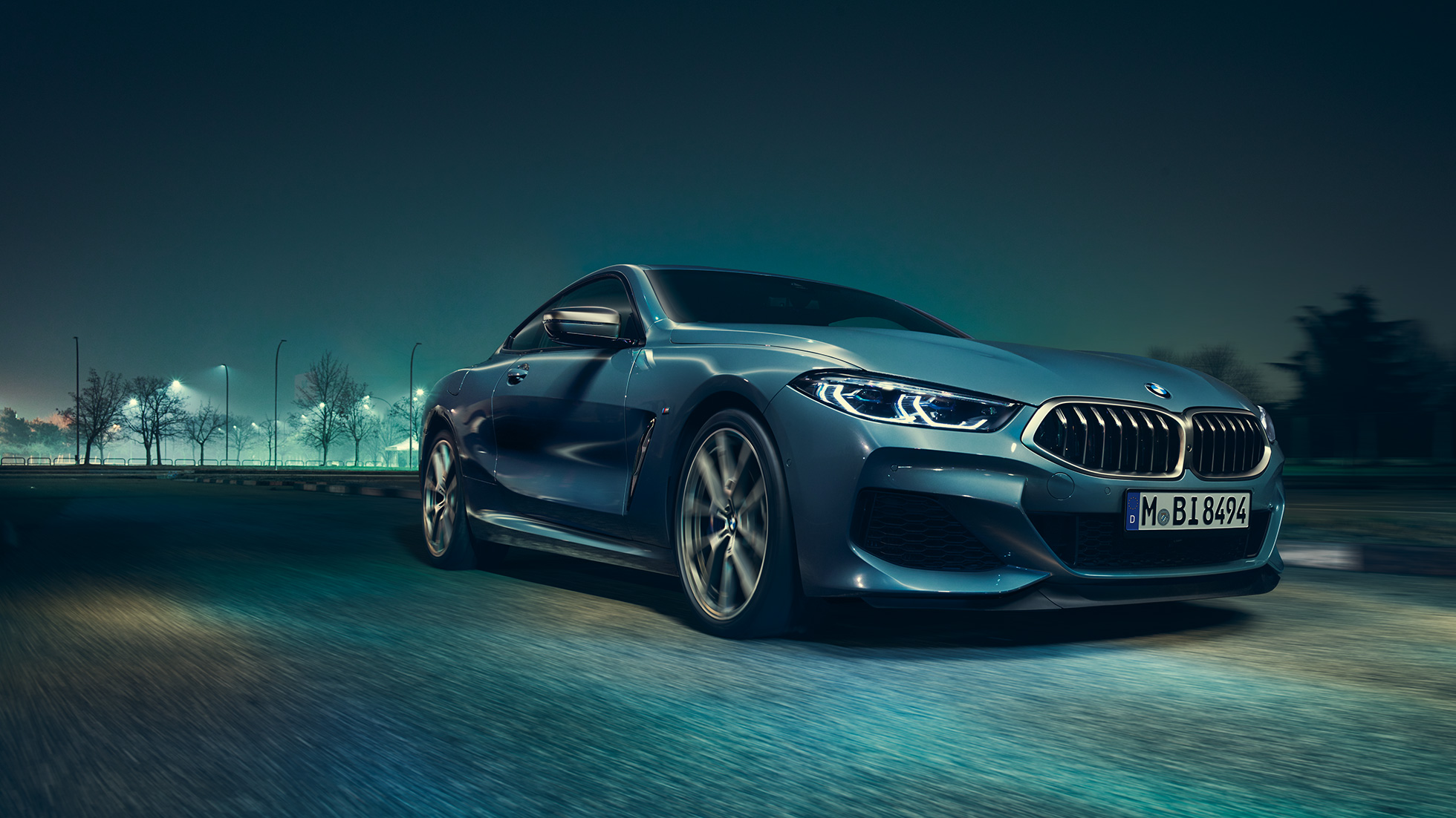 BMW M850i xDrive Купе, три четвърти изглед отпред вляво. BMW M850i xDrive Купе в Barcelona Blue metallic, три четвърти изглед отпред вляво в движение през нощта.