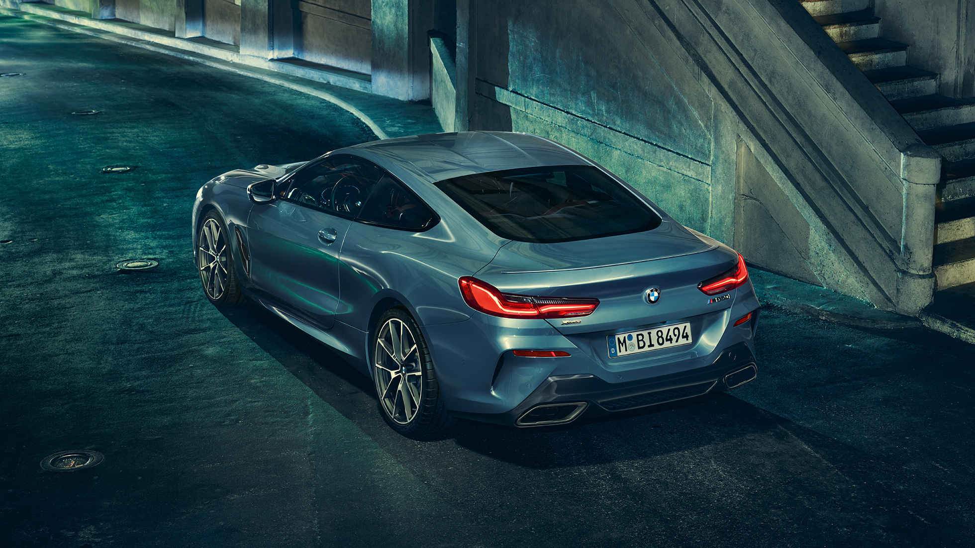 BMW M850i xDrive Купе, три четвърти изглед отзад отляво. BMW M850i xDrive Купе в Barcelona Blue metallic, три четвърти изглед отзад отляво в покой през нощта.
