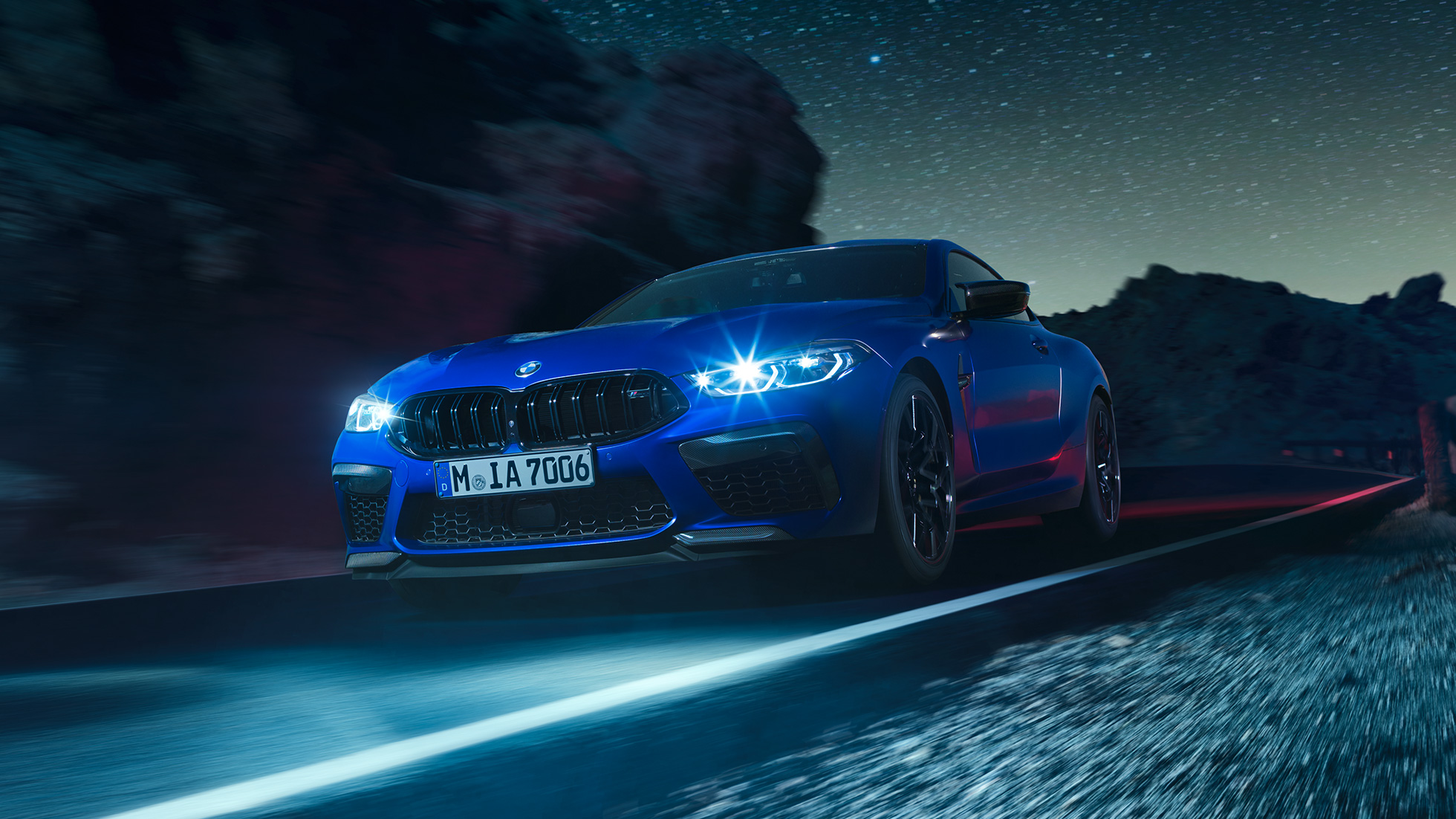 BMW M8 Competition Купе, три четвърти изглед отпред. BMW M8 Competition Купе в Marina Bay Blue metallic с ярки LED фарове, три четвърти изглед отпред в движение през нощта.