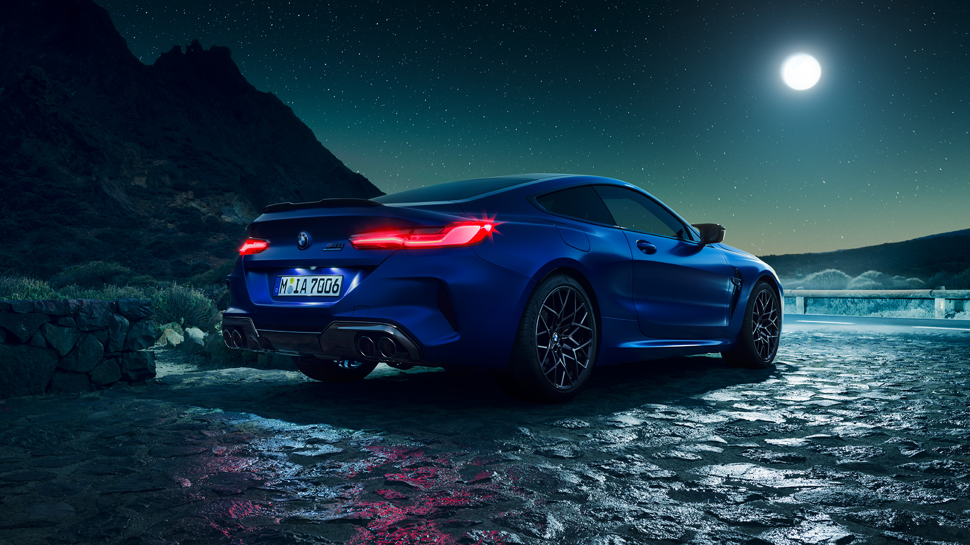 BMW M8 Competition Купе, три четвърти изглед отзад. BMW M8 Competition Купе в Marina Bay Blue metallic с ярки LED фарове, три четвърти изглед отпред в покой при пълнолуние.