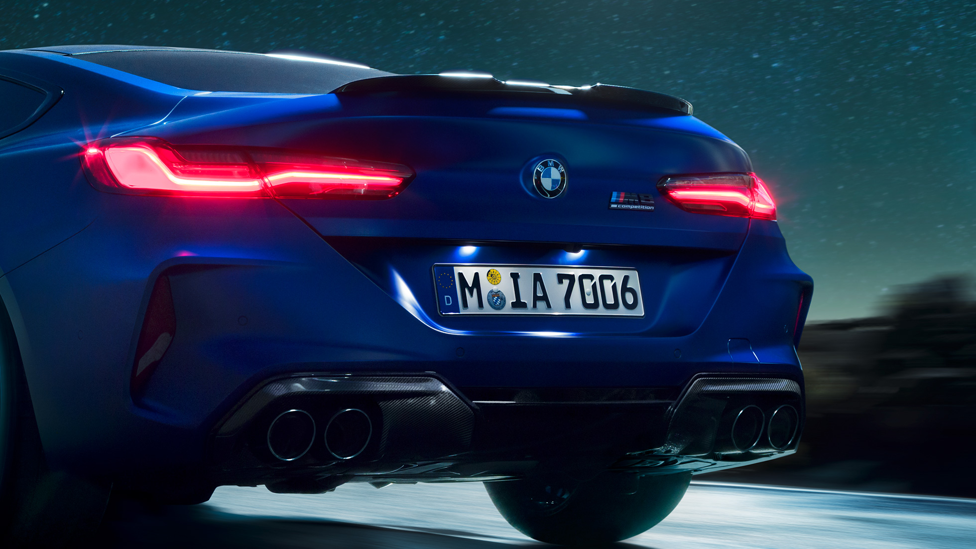 Черен карбонов М дифузор. BMW M8 Competition Купе в Marina Bay Blue metallic, снимка отблизо на задната част през нощта с черен карбонов М дифузор.