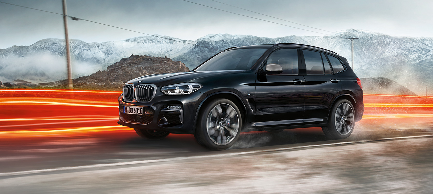 BMW X3 M40i и BMW X3 M40d, страничен изглед. BMW X3 M40i и BMW X3 M40d в цвят Black Sapphire metallic, в движение, екстериор, страничен изглед на фона на планински пейзаж със светлинни ивици.