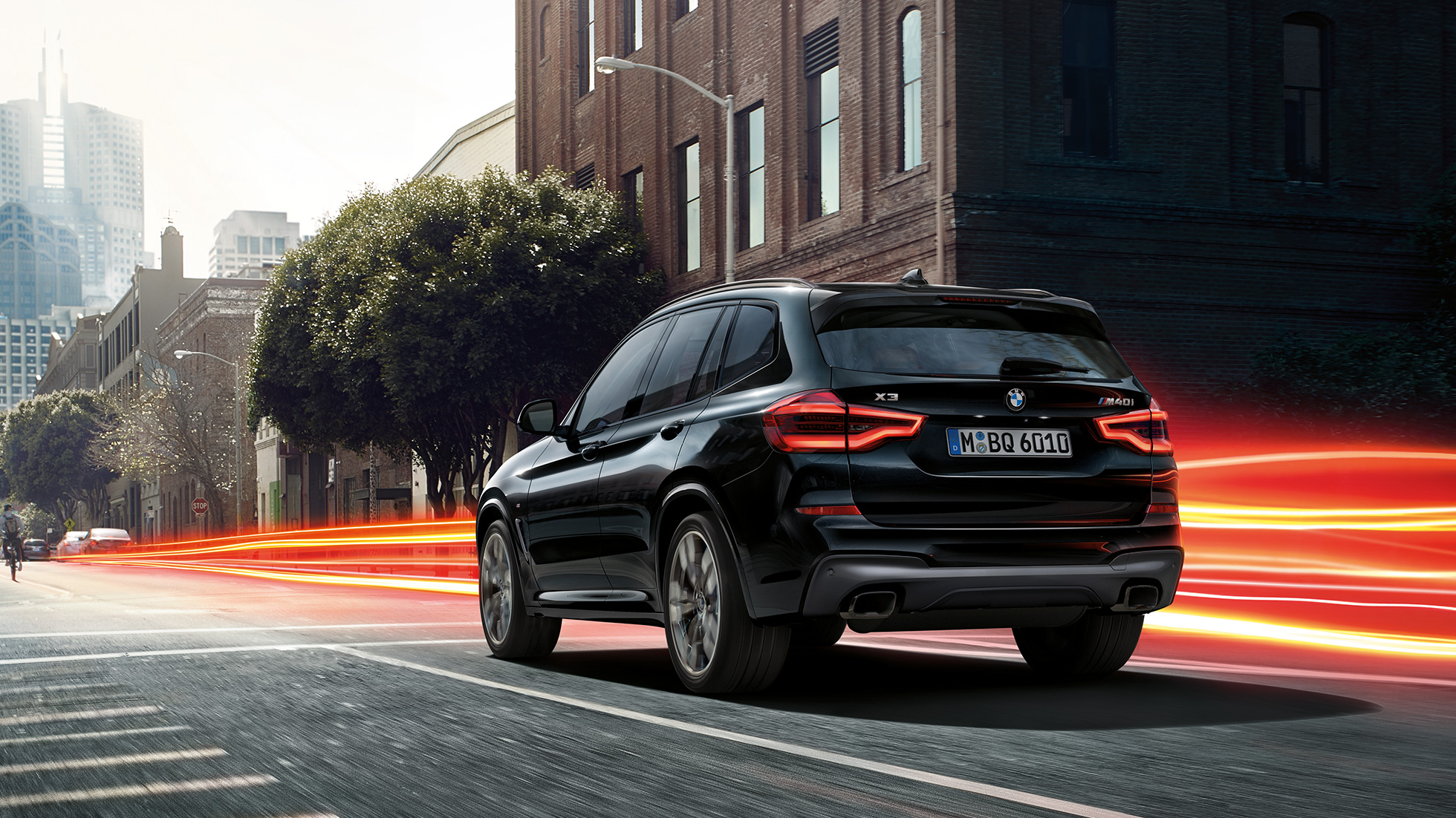BMW X3 M40i в цвят Black Sapphire metallic, три четвърти изглед отзад. BMW X3 M40i в цвят Black Sapphire metallic, в движение, екстериор, три четвърти изглед отзад на фона на града със светлинни ивици.