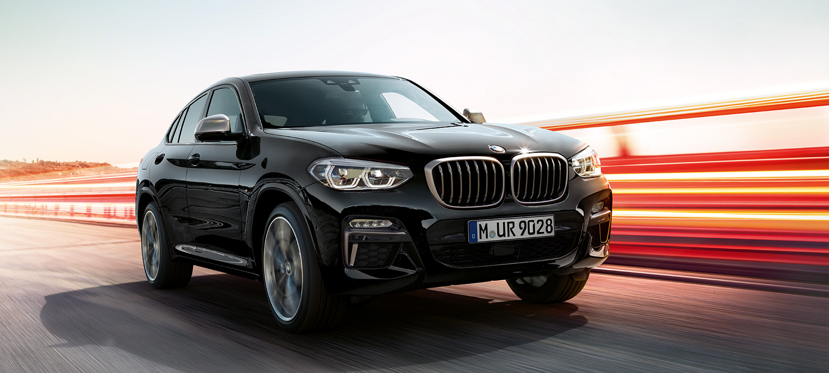 BMW X4 M40i и BMW X4 M40d, три четвърти страничен изглед отпред отляво. BMW X4 M40i и BMW X4 M40d в цвят Black Sapphire metallic, в движение, екстериор, три четвърти страничен изглед отпред отляво със светлинни ивици.