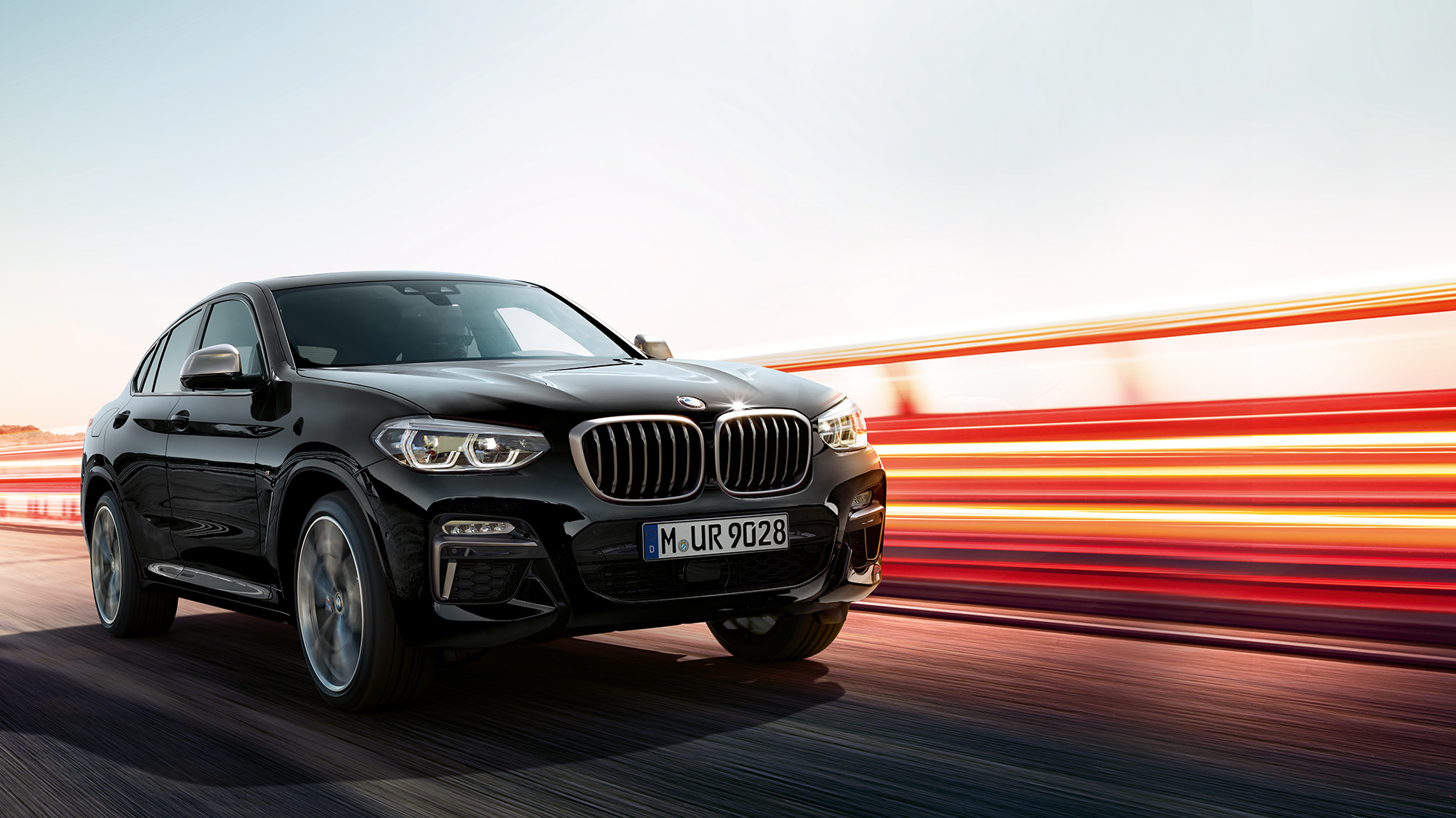 BMW X4 M40i, три четвърти изглед отзад. BMW X4 M40i в цвят Black Sapphire metallic, в движение, екстериор, три четвърти изглед отзад със светлинни ивици.