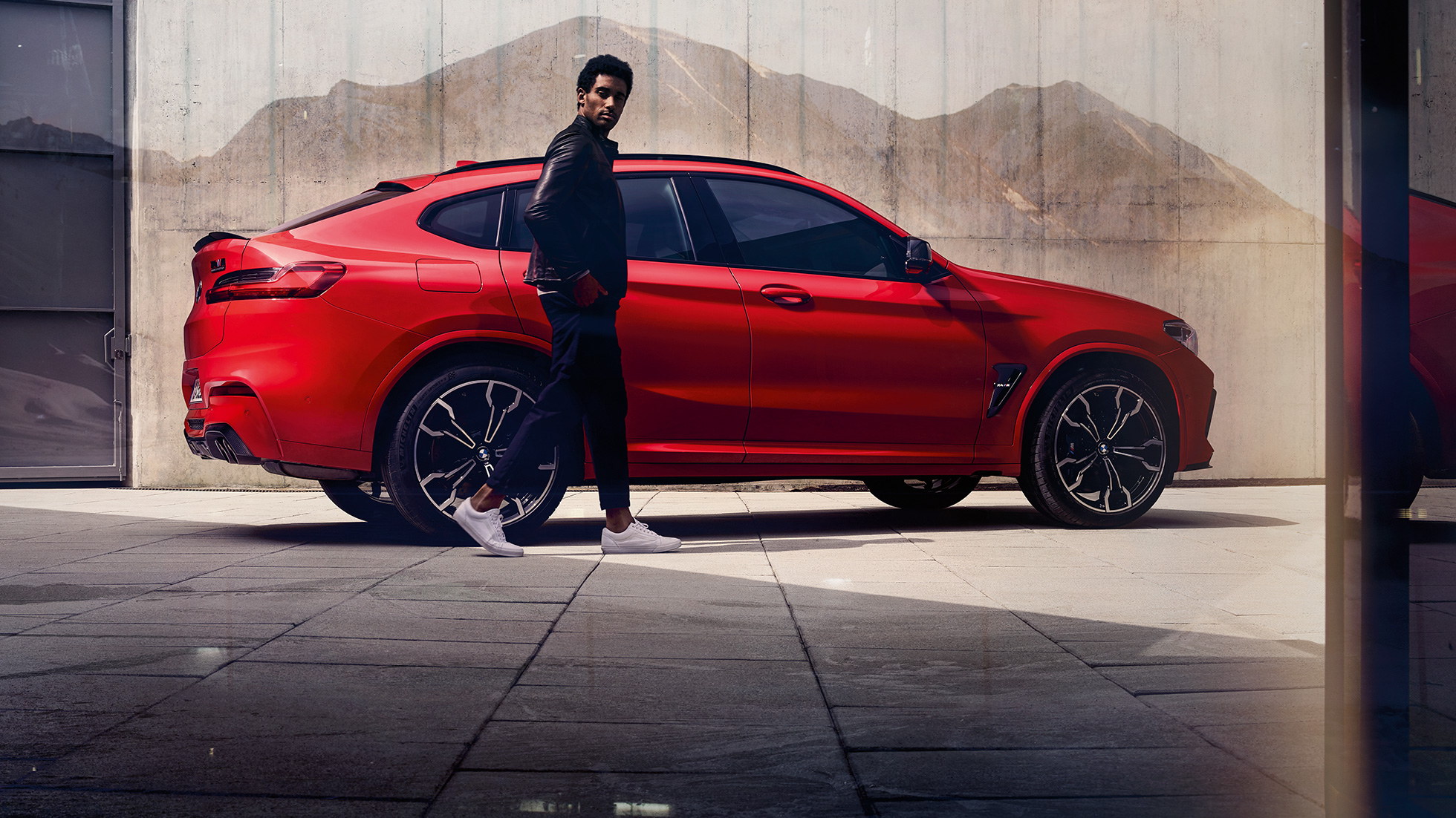 BMW X4 M Competition, изглед отстрани с млад мъж. BMW X4 M Competition в цвят Toronto Red metallic, екстериор, изглед отстрани с млад мъж.