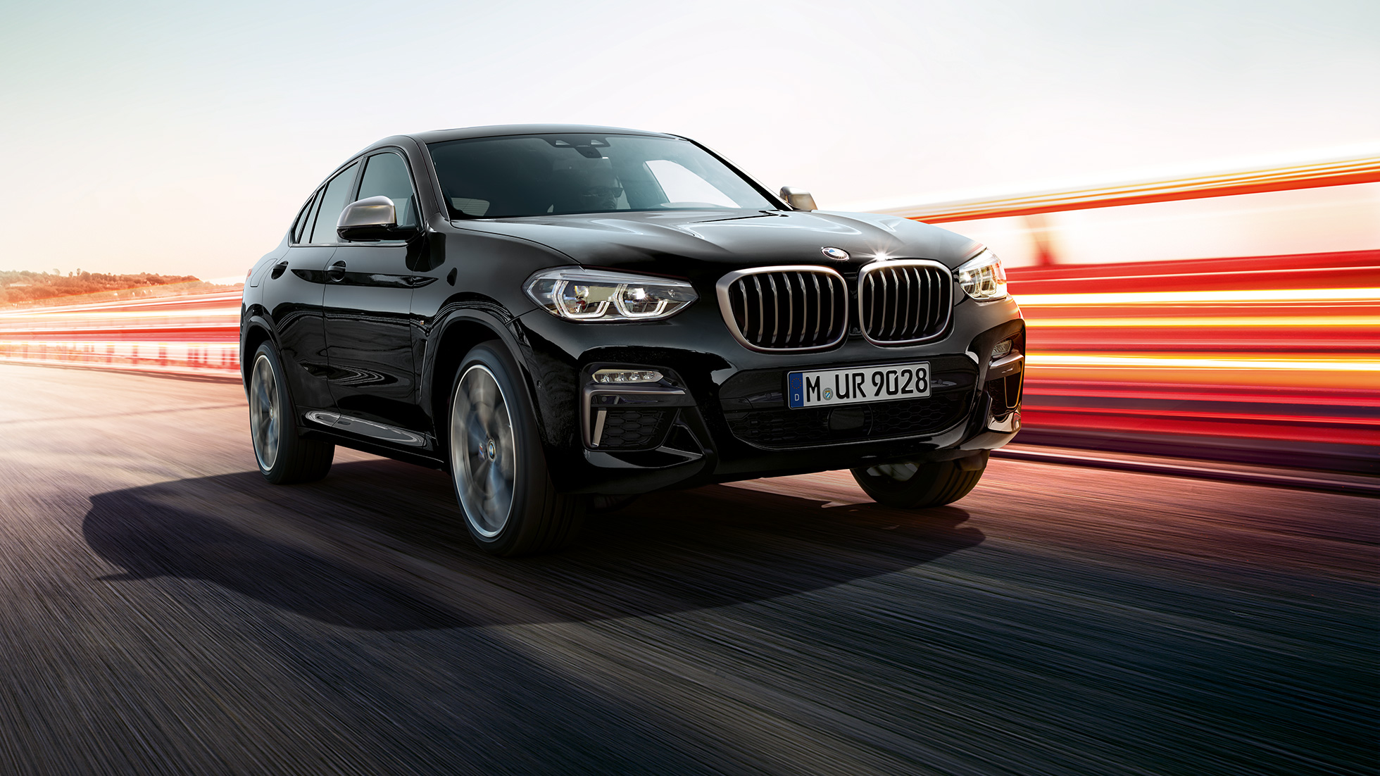 BMW X4 M40i и BMW X4 M40d, три четвърти изглед отпред. BMW X4 M40i и BMW X4 M40d в цвят Black Sapphire metallic, екстериор, три четвърти изглед отпред отляво със светлинни ивици.