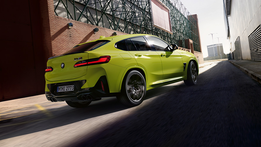 BMW X4 M Competition F98 LCI 2021 три четвърти изглед отзад BMW X4 M Competition F98 LCI Facelift 2021 Sao Paulo Yellow три четвърти изглед отзад между фабрични халета в движение
