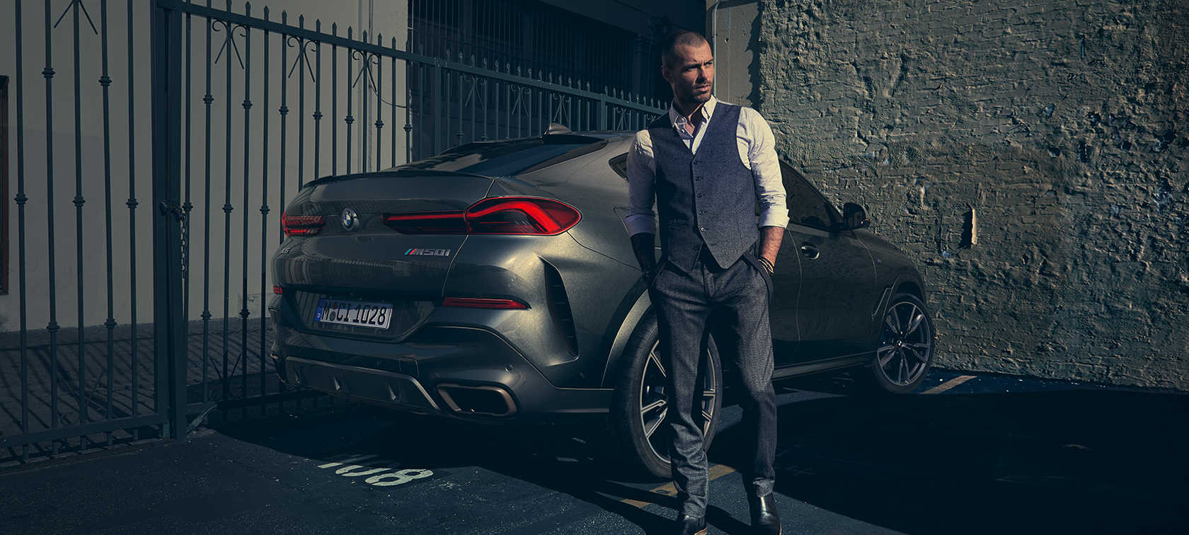 BMW X6 M50i три четвърти изглед отзад G06 Мъж стои до BMW X6 M50i G06 2018 SUV три четвърти изглед отзад