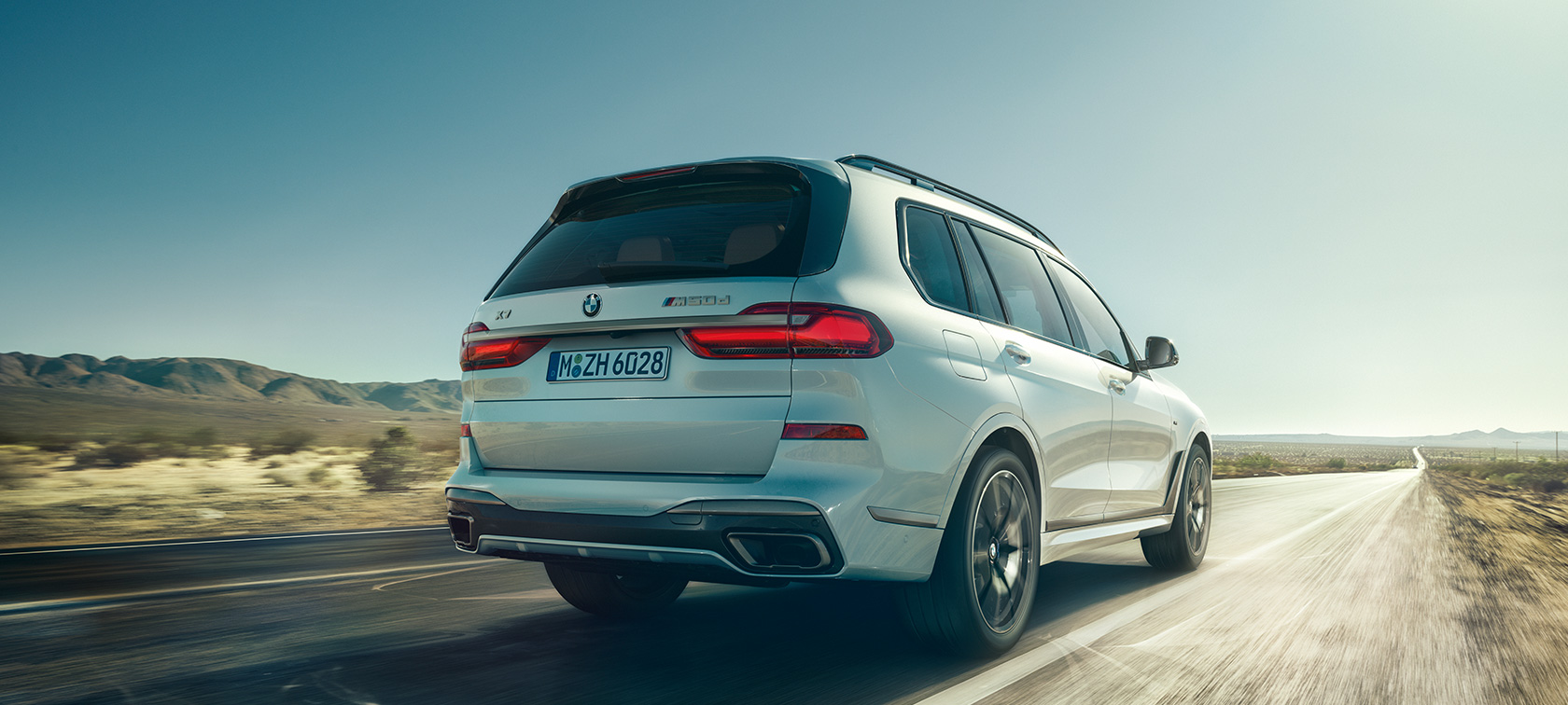BMW X7 M50d, изглед отзад BMW X7 M50d в цвят Mineral White, в движение по пуста магистрала, изглед отзад, G07, 2019