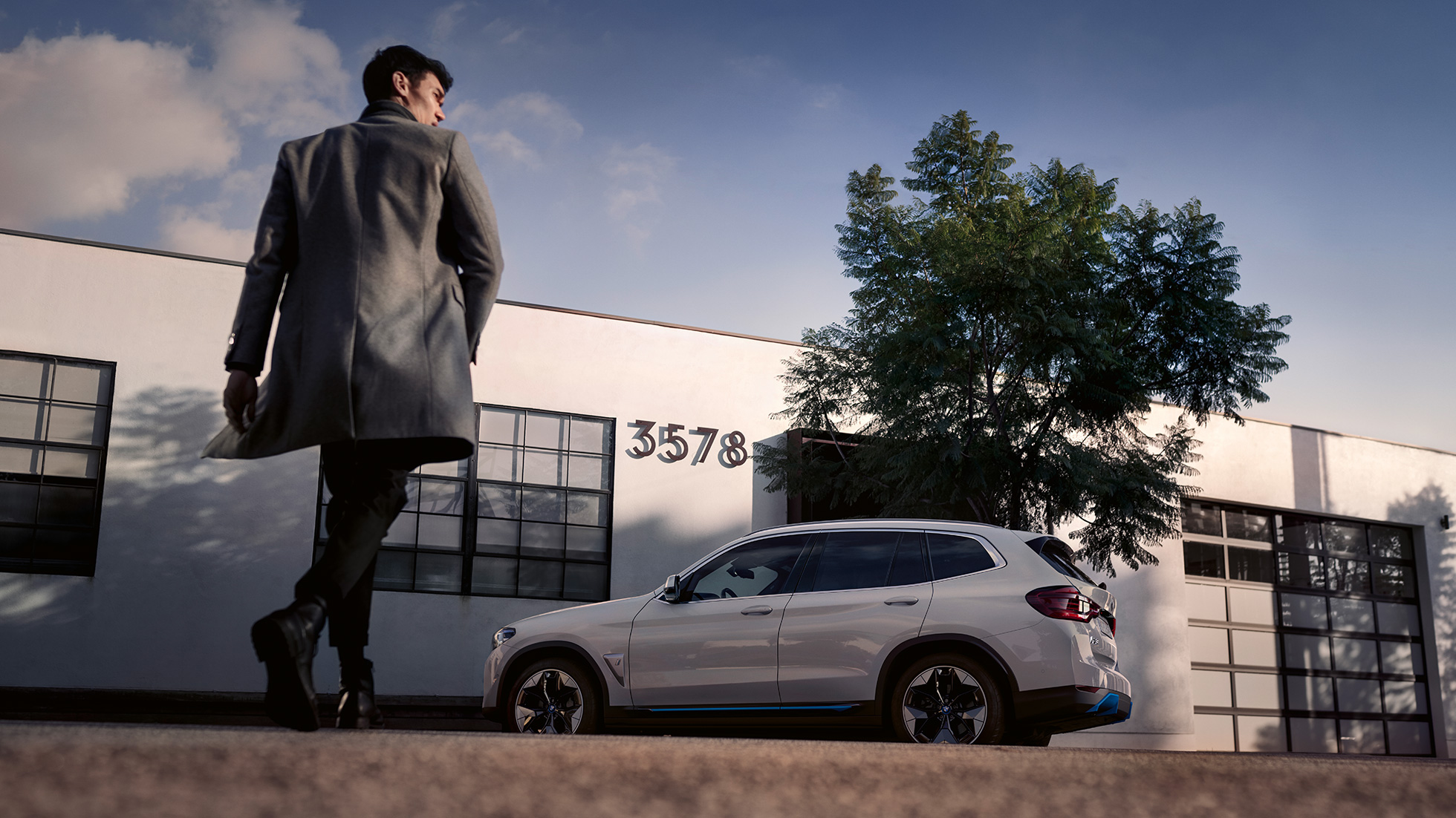 BMW iX3 G08 изглед отстрани пред сграда с мъж BMW iX3 G08 2020 Mineral White metallic изглед отстрани пред сграда с мъж