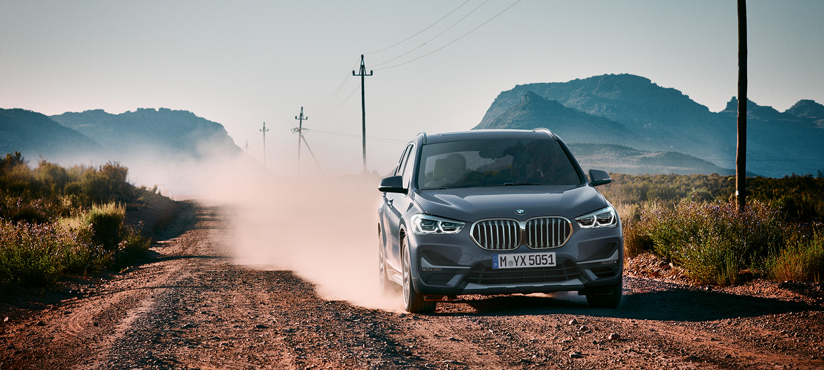 BMW X1, три четвърти изглед отзад. BMW X1, три четвърти изглед отзад, в движение на фона на планински пейзаж.