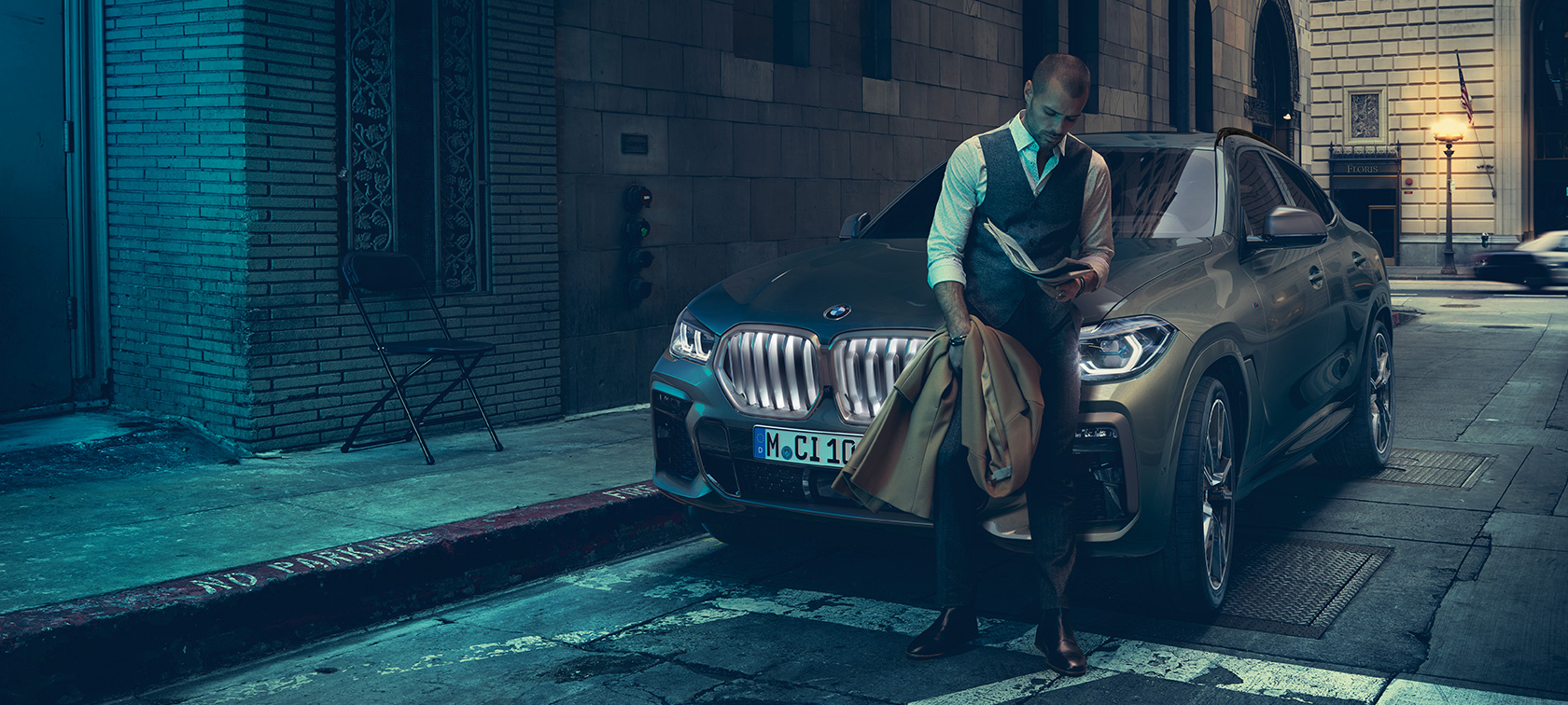 Мъж се обляга на BMW X6. Мъж се обляга на BMW X6, изглед отстрани на фона на градски рейзаж.