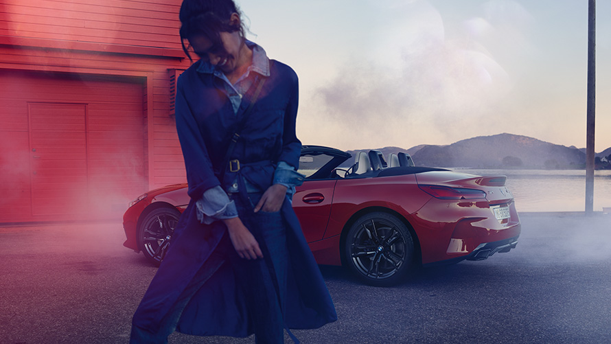 BMW Z4 M40i Роудстър G29 с отворен текстилен покрив BMW Z4 M40i Роудстър G29 три четвърти изглед отзад с отворен текстилен покрив и жена на преден план