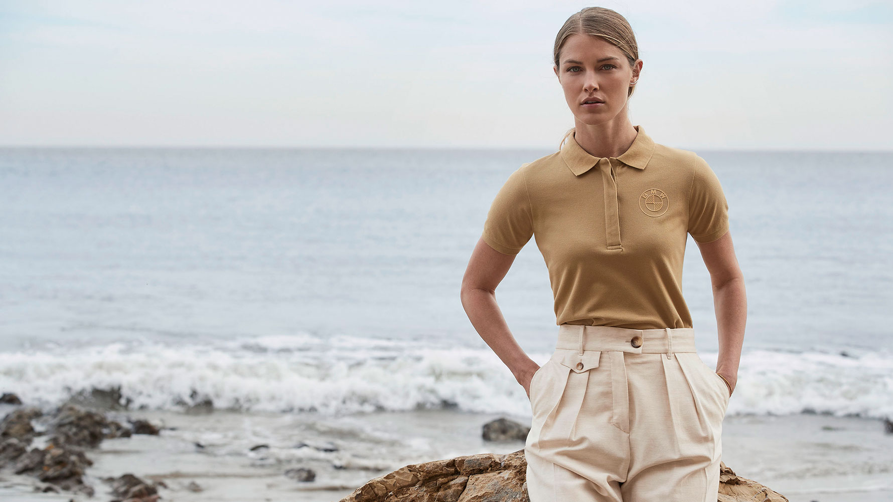 Eine junge Frau trägt das BMW Polo-Shirt Logo Damen vor einer Strand-Kulisse. Eine junge Frau trägt das BMW Polo-Shirt Logo Damen vor einer Strand-Kulisse.