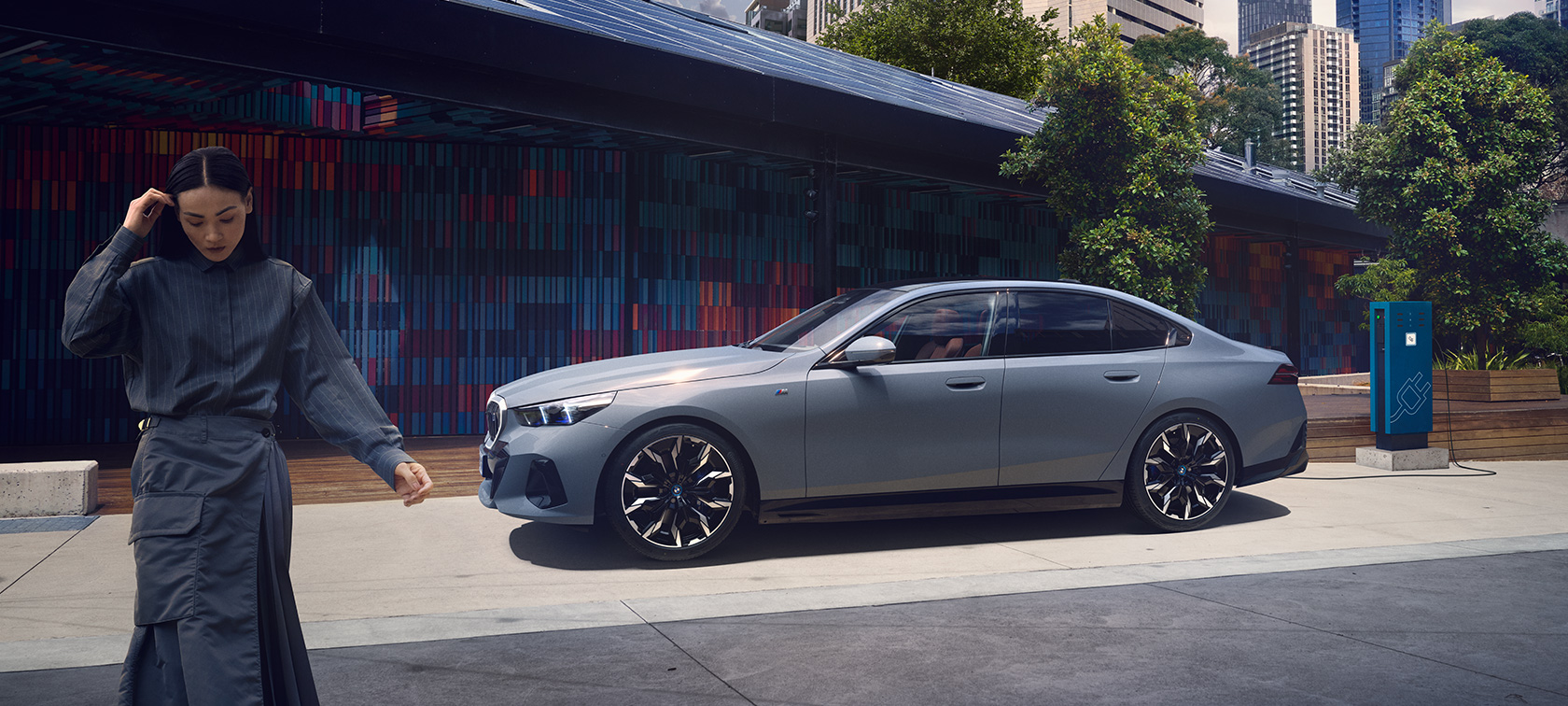 BMW i5 G60изглед отстрани при зареждане BMW i5 G60изглед отстрани с жена при зареждане
